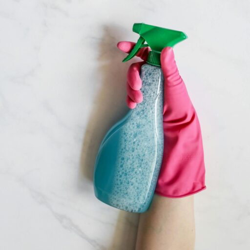 Close-up image of a hand in a pink glove holding a spray bottle against a white background.
